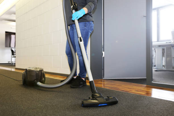 A woman using a vacuum cleaner to clean a carpet, representing commercial carpet cleaning services.