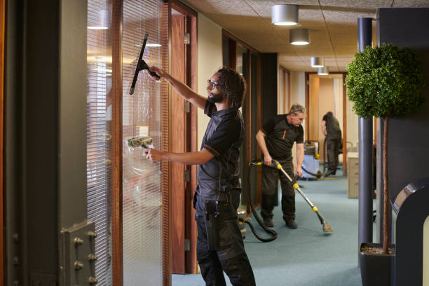 A man using a vacuum to clean a glass door in a commercial cleaning service setting.