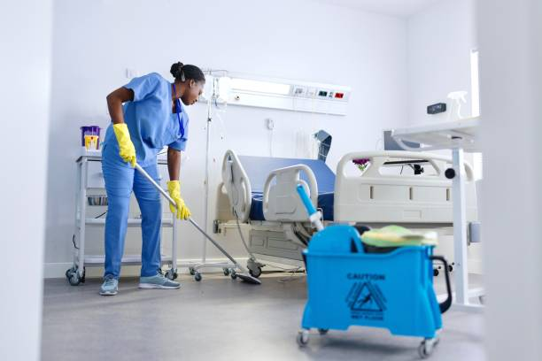 A person wearing white gloves cleans a hospital bed in a medical office setting, ensuring a sterile environment. 