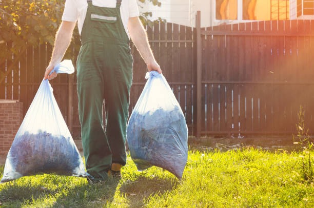 A man in overalls stands holding two bags of garbage, ready for disposal in a floor cleaning context.
