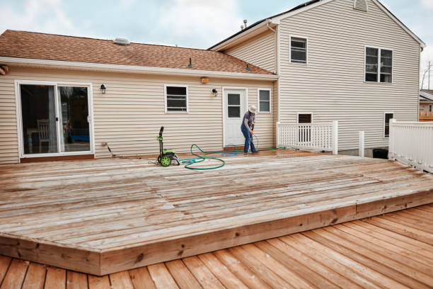 A man cleans a wooden deck with a hose, focusing on floor cleaning and maintenance.