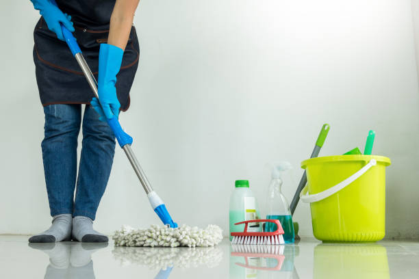 A woman mops the floor, focusing on cleaning a large area with a determined expression.