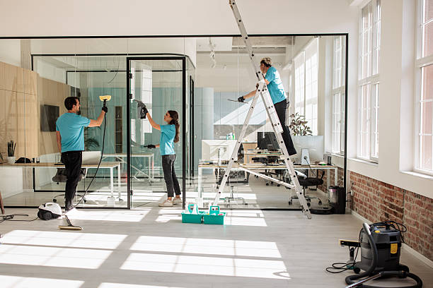 Two people cleaning a glass wall in an office, focusing on post-construction cleaning tasks.