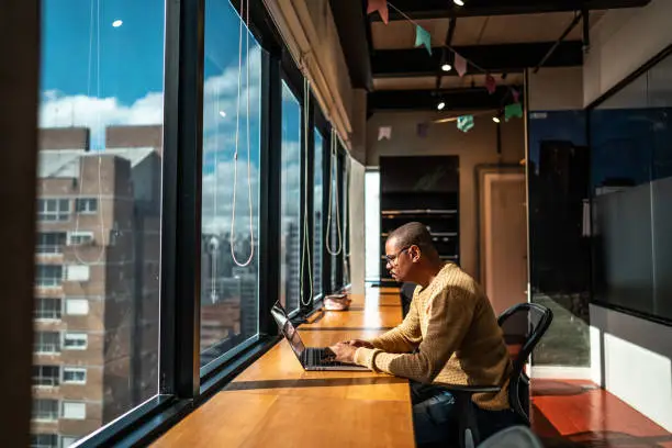 A man sitting at a desk, illuminated by natural light streaming through an office window.