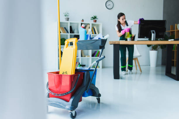 A woman using a cart of cleaning supplies to clean a room, representing commercial cleaning services.