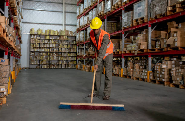 A worker sweeping the floor of a warehouse, focusing on maintaining cleanliness in the storage area.