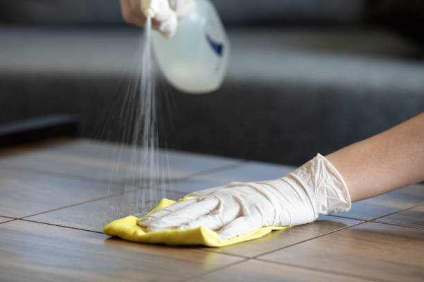 A man wearing blue gloves cleans an air conditioner as part of daily office cleaning duties.