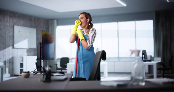 A woman in an apron and rubber gloves cleans a desk as part of her daily office cleaning routine.