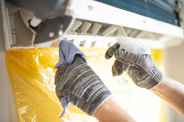 A person wearing gloves cleans an air conditioner as part of daily office cleaning tasks.