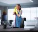 A woman in an apron and rubber gloves cleans a desk as part of her daily office cleaning routine.