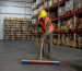 A worker sweeping the floor of a warehouse, focusing on maintaining cleanliness in the storage area.